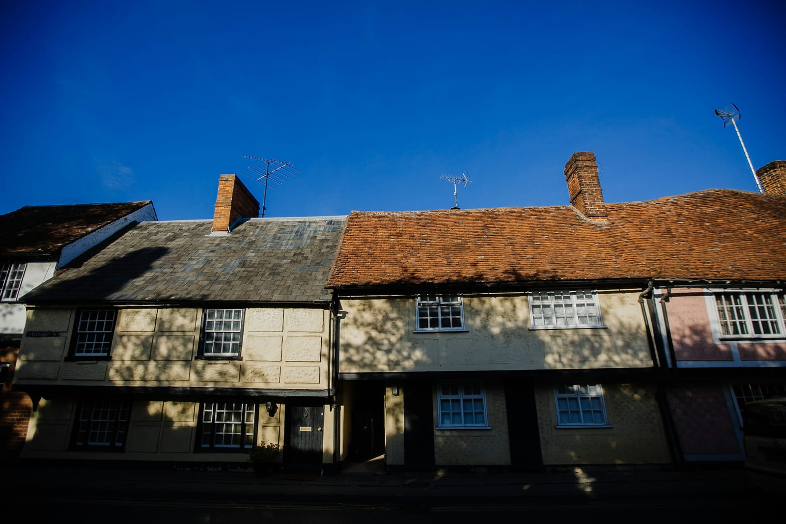 A street of old timber-framed cottages with decorative pargeted plasterwork, small leaded windows and steep clay-tiled roofs.