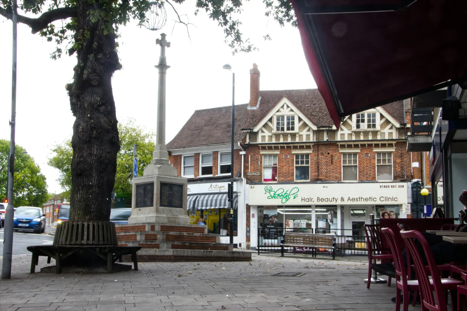 Suburban high street around a war memorial and a mature tree, a London street where a large tree shapes what can be built nearby