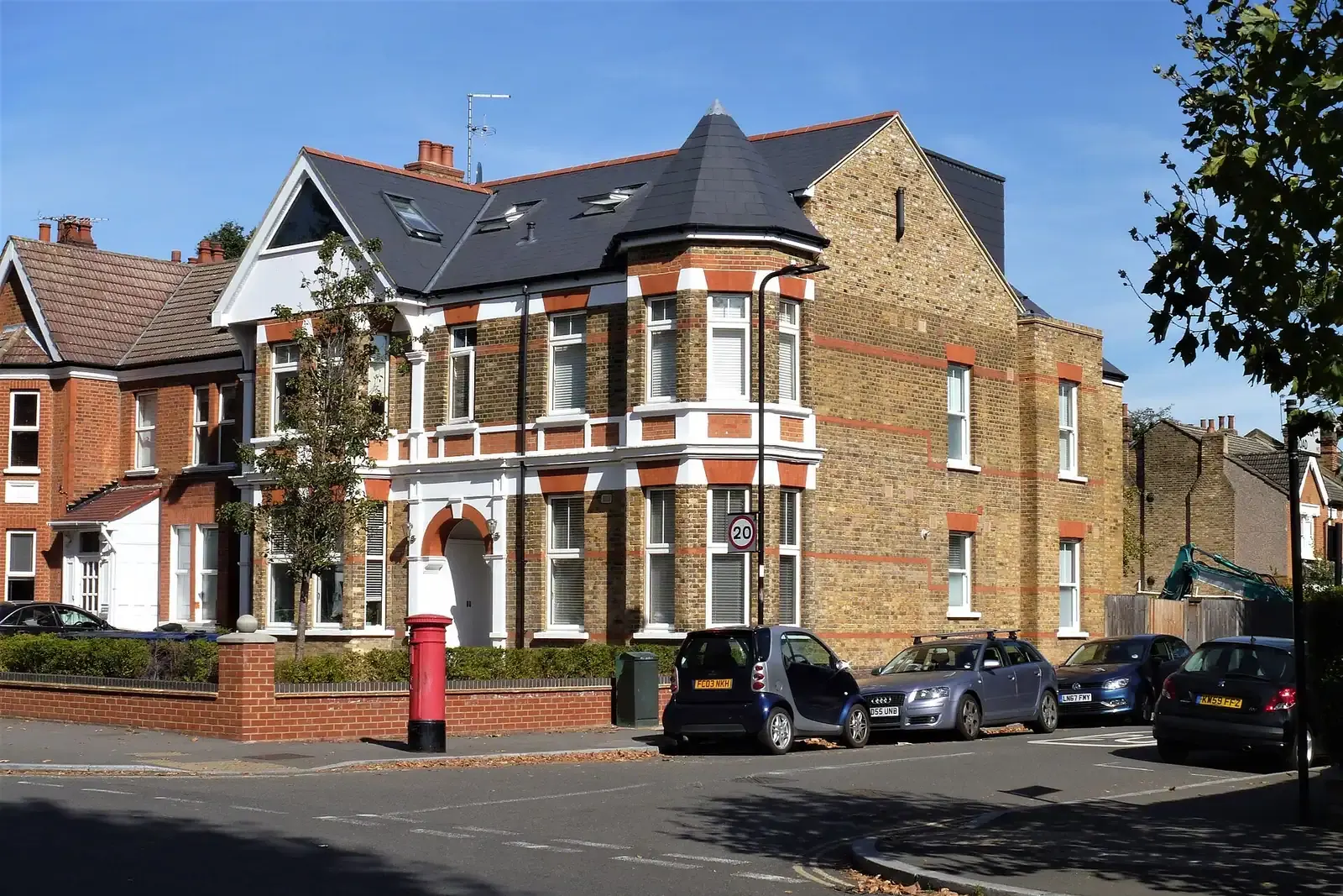 Large Edwardian corner house in Ealing with a turret, white bay windows and new roof windows in a dark slate roof, a red post box beside it