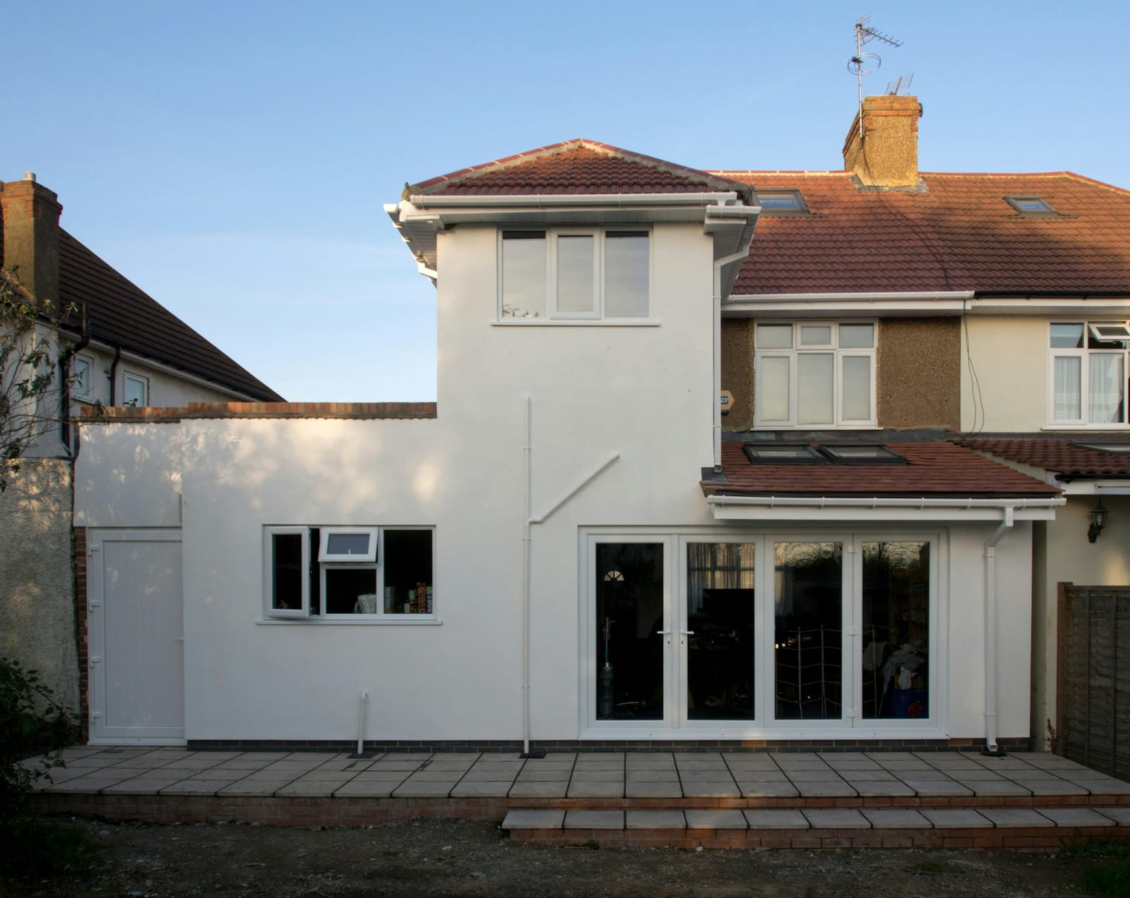 Rear of a pebbledashed semi with a new white-rendered single-storey extension, white bifold doors, two rooflights and a paved patio