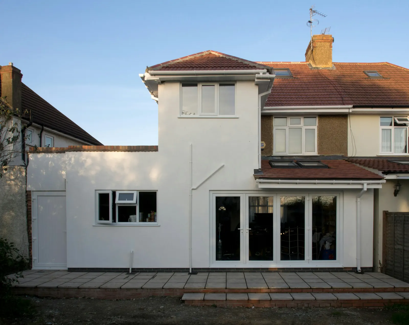 Rendered single-storey rear extension with French doors and a small first-floor addition on the back of a semi-detached London house