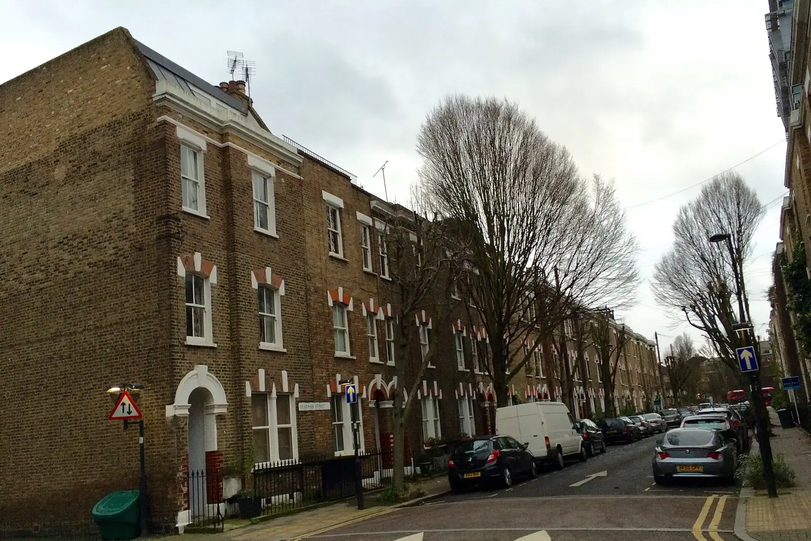 Corner of yellow-brick Victorian terraced houses with red brick arches on Pearman Street in Lambeth, a white van and plane trees