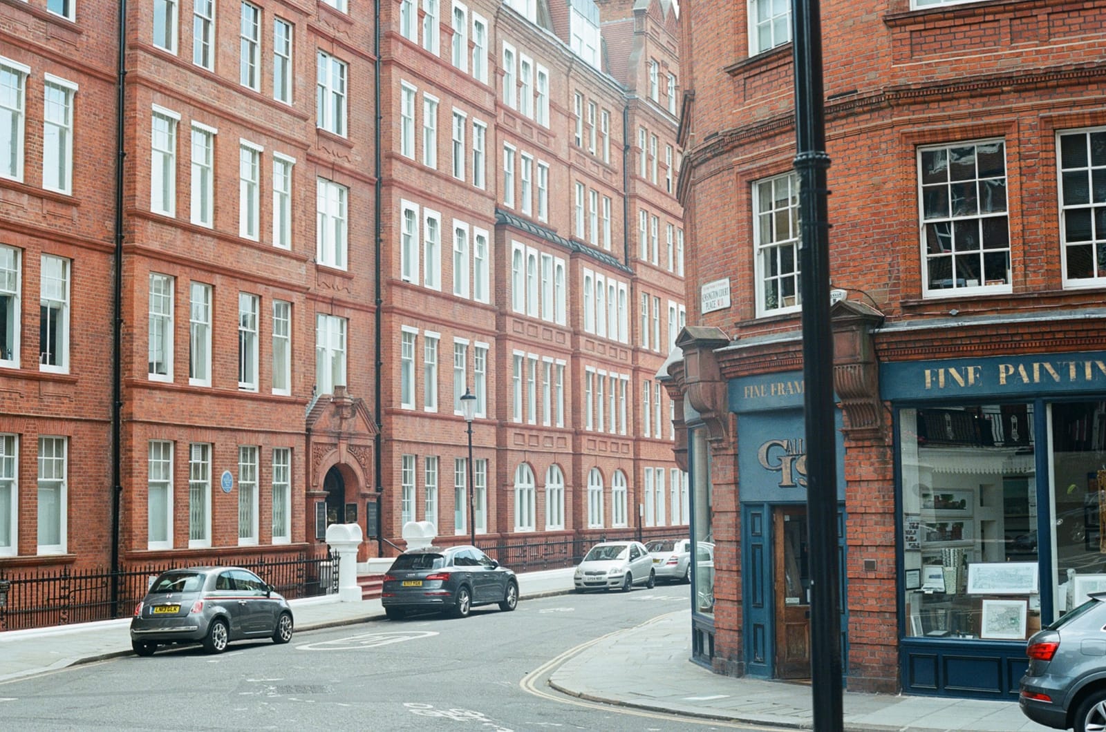 Red-brick Victorian mansion blocks with white sash windows on a quiet London street, cars parked at the kerb