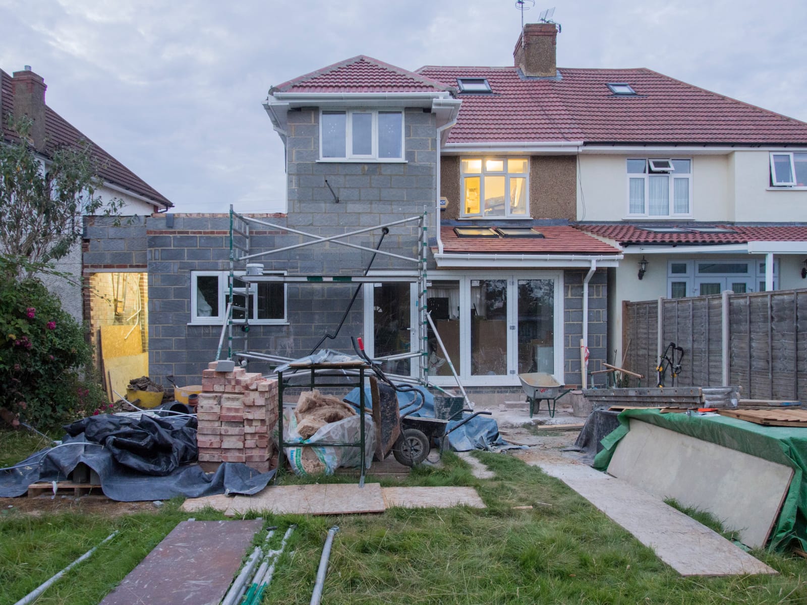 Semi-detached house with a new two-storey blockwork addition to the side and rear, tiled roof on, scaffold tower and bricks in the garden